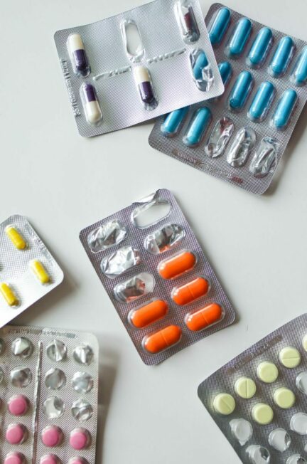 ALD maladies / Various blister packs of colorful pills and capsules on a white surface.