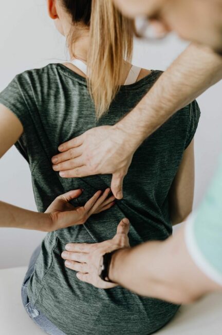 spondylarthrite ankylosante / Top view of crop unrecognizable woman in casual wear showing chiropractor in eyeglasses and uniform pain spot on back while sitting on examination couch in hospital