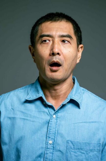 Le choc du diagnostic / Close-up portrait of a surprised Asian man wearing a blue denim shirt, expressing shock.