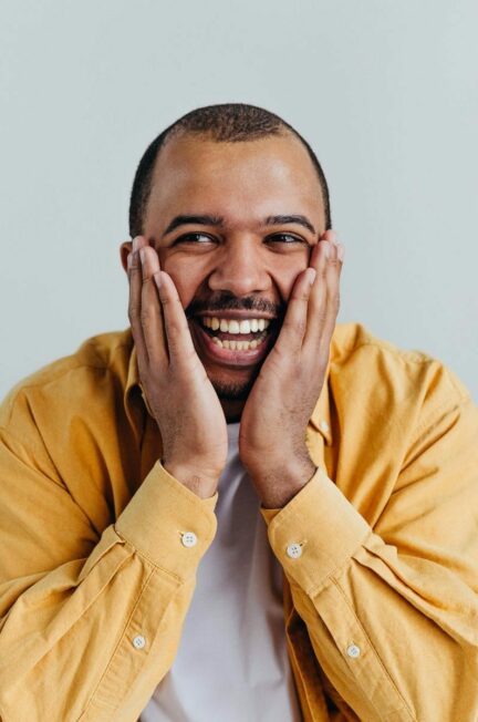 pas l'air malade / Happy African American man smiling with hands on face in studio shot.