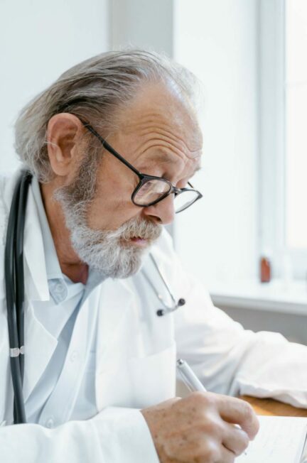 médecin traitant / Senior doctor with eyeglasses writing notes during consultation indoors.