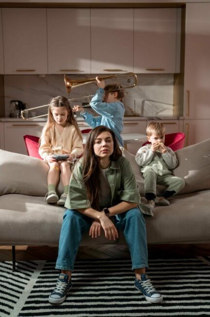 Faire des enfants en ayant une maladie chronique / A mother sits with her children playing indoors on a sofa in a modern living room.