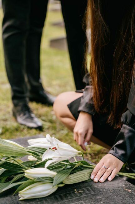deuil ancien soi / A woman kneels by a grave adorned with white lilies, symbolizing loss and remembrance.